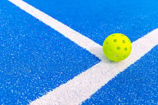 A close up of a plastic pickleball on the corner of the court ready for a game recreational sport concept photo