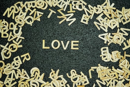 Wooden letters forming love surrounded by scattered letters on black mat photo