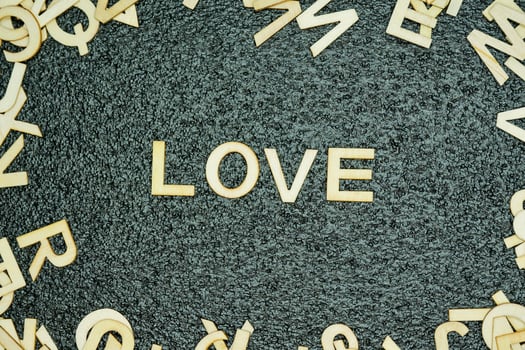 Wooden love letters on black rubber mat with scattered letters around photo