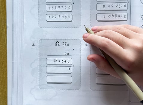 A young student sits at a wooden desk working on basic math exercises, steadily developing essential problem solving skills.e photo
