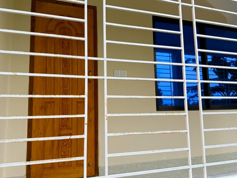 Rustic white metal bars guard the home's ornate wooden door and tinted window exterior photo