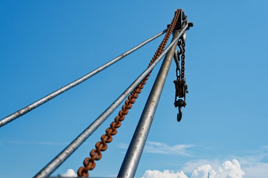 Rusty metal crane with heavy chain and hook against blue sky in Copenhagen CPH photo