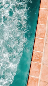 Aerial view shows shimmering light patterns dancing on turquoise pool water next to terra cotta tiles photo