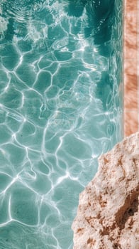 Turquoise pool water shows sunlight patterns with stone border, creating a summer vibe in the bright sun photo