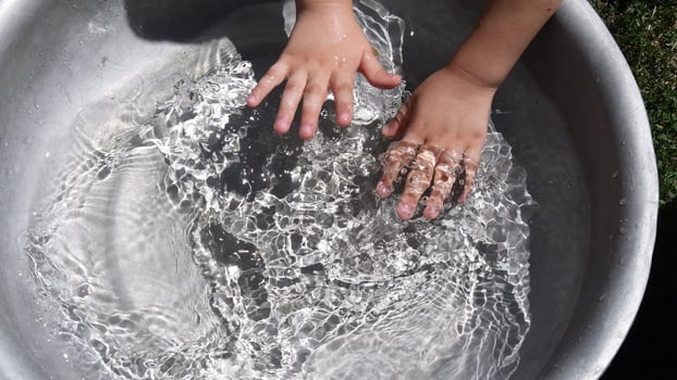 Kid washing hands in clear water inside basin. Summer fun photo