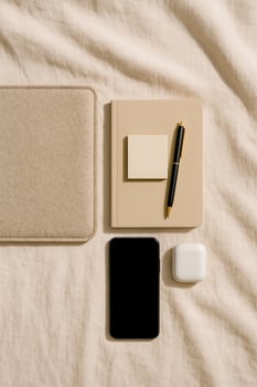 Notebook with sticky note, phone and earbuds case on linen with laptop sleeve, warm light minimal workspace photo
