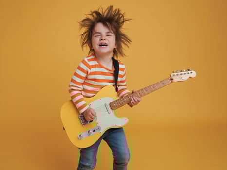 Young child with messy hair playing electric guitar, expressing joy against a vibrant yellow background. photo