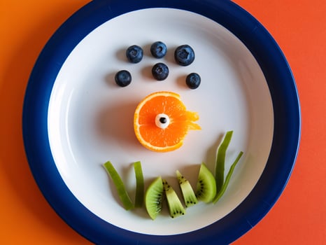 A colorful arrangement of fruit on a white plate against a bright orange background. photo