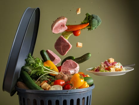 An artistic display of food waste with vegetables and meat falling into a trash can against a green background. photo
