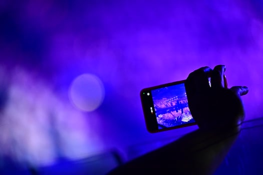 Young girl filming concert with phone in bright neon pink lighting photo
