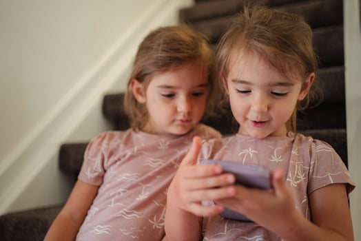 Two preschool age girls using a smartphone sitting on stairs at home photo