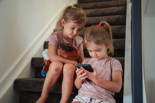 Two young sisters using a smartphone sitting on stairs at home photo