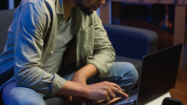 Black freelancer taking notes on textbook in order to solve his tasks, doing research and studying articles online. Young adult enjoying remote job and relaxed schedule, telework. Camera B. photo