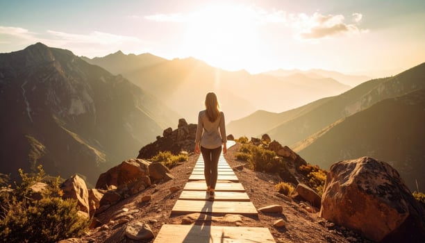 Person walks along wooden path through mountainous landscape during sunset, surrounded by rocky terrain and lush greenery. warm sunlight creates serene and peaceful atmosphere, inviting photo