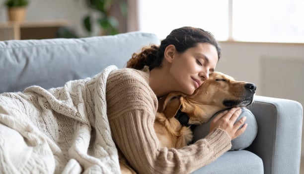 Woman relaxes on couch, embracing golden retriever dog. They share peaceful moment together, wrapped in cozy blanket, showcasing warmth and companionship photo