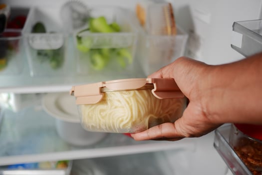 Hand holding a container of pasta in a refrigerator photo