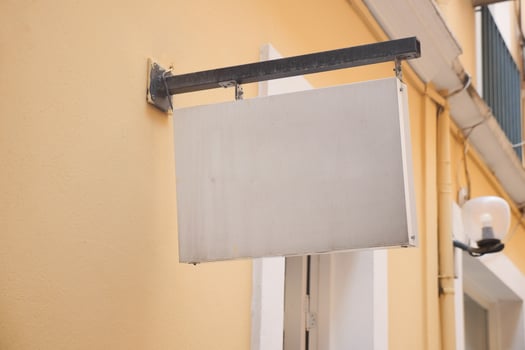 Blank sign hanging on a yellow wall in a quiet alley photo