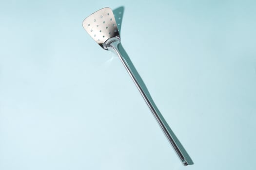 Stainless Steel Perforated Spatula on a Light Blue Background photo