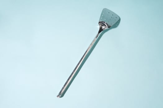 Chrome Stainless Steel Perforated Spatula on a Light Blue Background photo