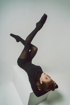 young ballerina, in a black dress and total black sunglasses lies on her back with her legs raised photo