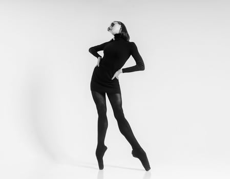 a young ballerina in a black dress and sunglasses total black, demonstrates choreography, on pointe shoes. photo