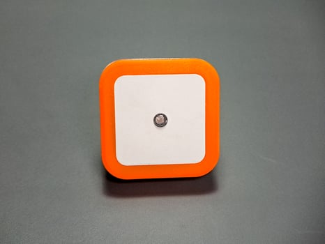 A geometric object with a rounded square form showcases modern simplicity on a neutral background, highlighting the interplay of white, orange, and a dark grey backdrop. photo