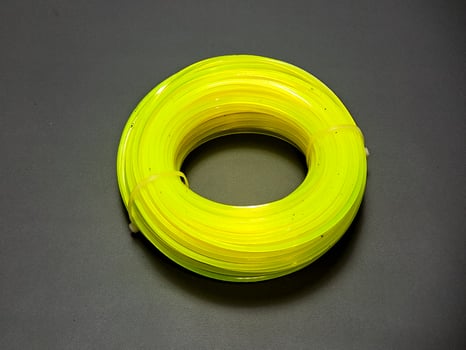A vibrant coil of yellow lawn trimming line rests upon a dark gray surface, forming a circular shape in the composition, ready for its intended purpose in garden care. photo