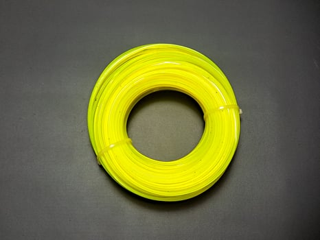 Coil of bright yellow trimmer line rests on a textured dark surface, presenting a vibrant, circular form with subtle light interplay, evokes sharpness and preparedness. photo