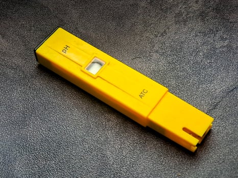 A yellow pH meter rests on a textured surface, with pH and ATC labeled on its body, used for scientific measurement and monitoring liquid acidity with ease and precision. photo