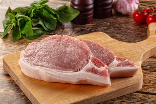 Two raw pork chops on a cutting board with herbs and vegetables photo
