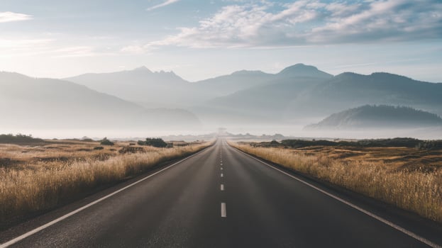 long shot of straight asphalt road stretching through mountains and fields photo
