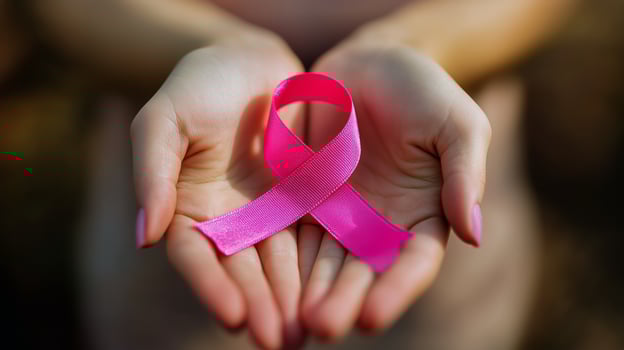 Hands Holding a Pink Ribbon Symbolizing Breast Cancer Awareness During a Sunny Day in a Natural Setting photo