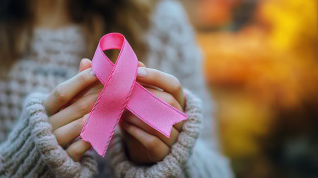 Hands Holding a Pink Ribbon Symbolizing Breast Cancer Awareness During a Sunny Day in a Natural Setting. photo