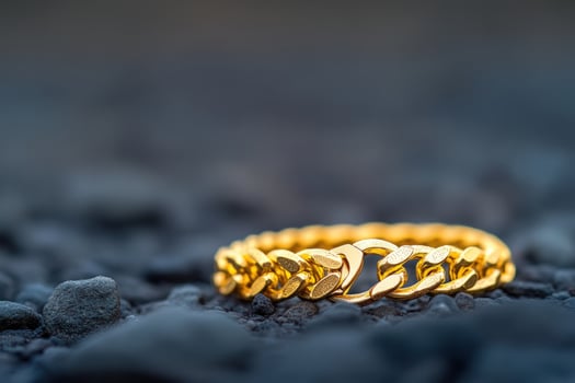 Gold chain bracelet rests on dark stones, blurred background photo