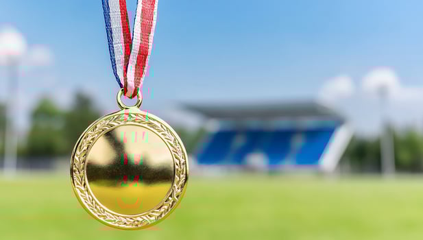 Gold medal award hanging on ribbon with sports field and blue sky background photo