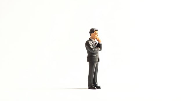 Miniature businessman in suit contemplates with hand on chin on white background photo