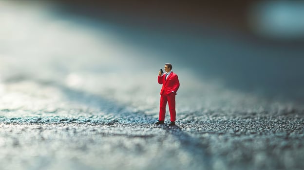 Miniature man in a red suit confidently uses his phone on a textured surface photo