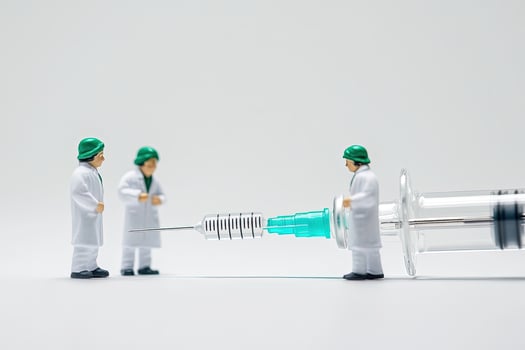 Three miniature toy doctors examine an outsized needle on a seamless white background photo