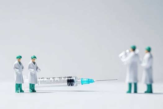 Miniature doctors in white coats observe a large syringe on a plain white background photo
