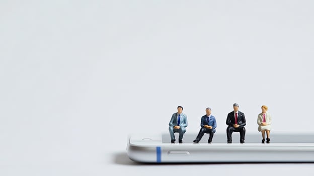 Four miniature figures sit on a modern white phone against a plain light backdrop photo