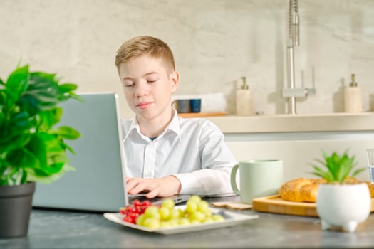 young boy, teenager plays on the notebook during breakfast time. Addiction to gadgets. Breakfast before school in the kitchen. photo