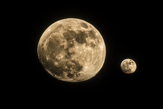 The moon and a small moon are shown in the dark photo