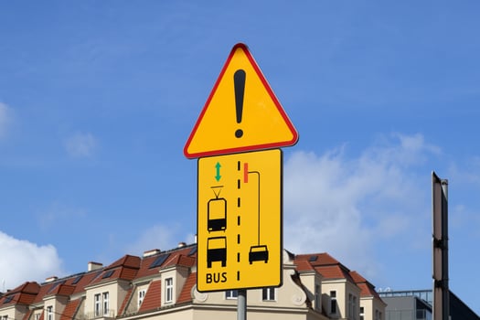 Yellow road sign with exclamation mark warns of complex traffic, depicting tram, bus, and car lanes for public transport rules, displaying BUS I text photo