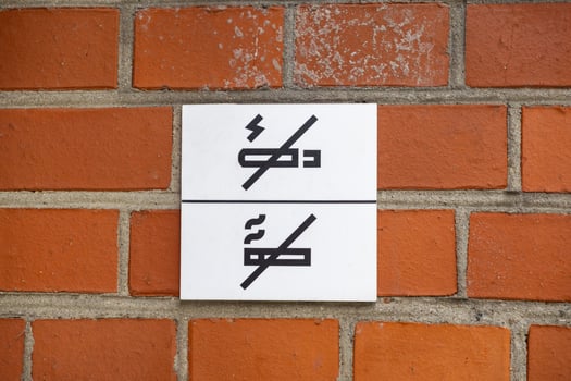 A prominent white sign displaying no smoking and no open flame symbols affixed to a textured red brick wall, indicating safety regulations for public areas photo