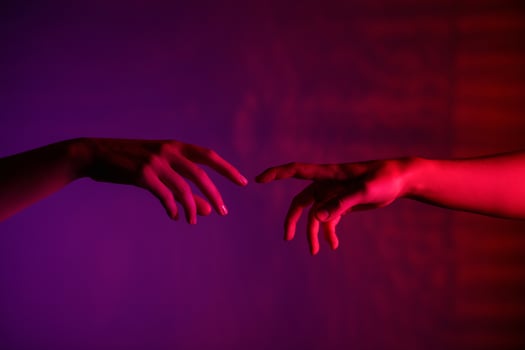 Two hands reaching towards each other under a purple-pink light, symbolizing connection and intimacy. photo
