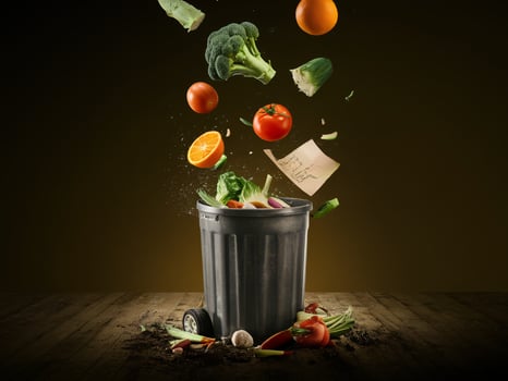 Colorful vegetables and fruits being tossed into a black trash bin against a dark background. photo