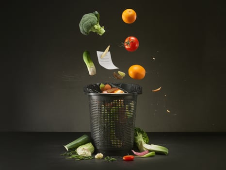 Colorful vegetables and fruits tossed into a black trash bin on a dark background. photo