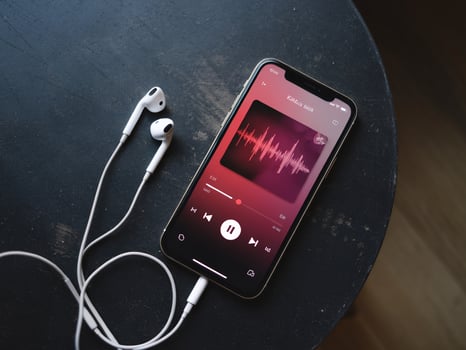 A smartphone with earphones resting on a dark table, displaying a music app interface. photo