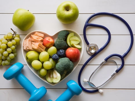 Healthy lifestyle essentials green fruits, broccoli, dumbbells, and a stethoscope on a wooden background. photo