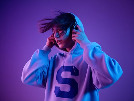 Young woman enjoying music in a stylish hoodie against a vibrant purple backdrop. photo